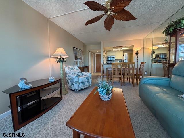 living area featuring carpet flooring, ceiling fan, and a textured ceiling