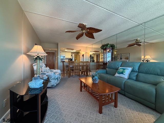 living area featuring carpet flooring, ceiling fan, and a textured ceiling