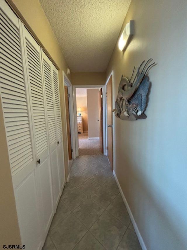 hall featuring baseboards, a textured ceiling, and tile patterned floors