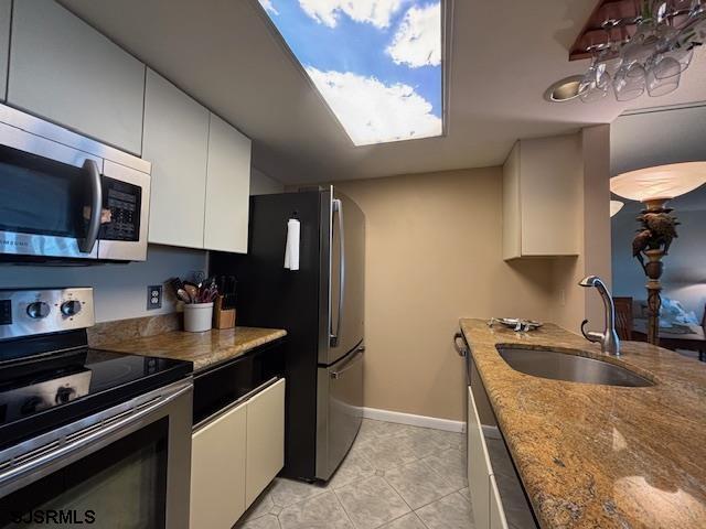 kitchen with white cabinetry, sink, dark stone countertops, light tile patterned floors, and appliances with stainless steel finishes