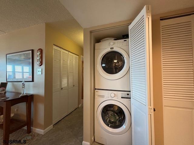 clothes washing area featuring stacked washer / drying machine, a textured ceiling, tile patterned flooring, laundry area, and baseboards