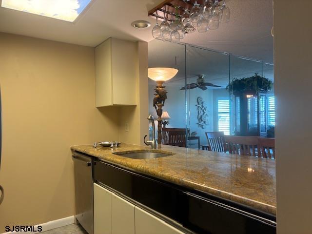 kitchen featuring stone counters, a sink, white cabinetry, a ceiling fan, and stainless steel dishwasher