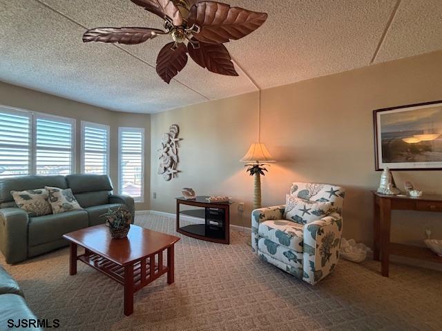 carpeted living area with a ceiling fan, a textured ceiling, and baseboards