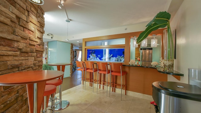 bar featuring light tile patterned floors, hanging light fixtures, and stainless steel refrigerator