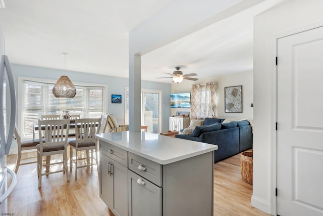 kitchen with light wood-type flooring, ceiling fan, decorative light fixtures, gray cabinets, and a kitchen island