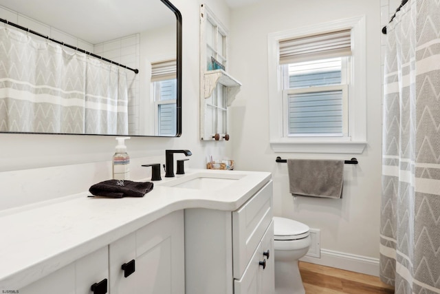 bathroom featuring wood-type flooring, vanity, toilet, and a healthy amount of sunlight