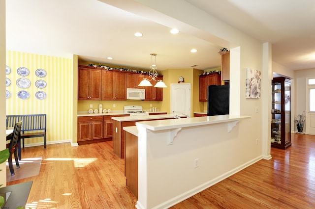 kitchen with pendant lighting, a breakfast bar, white appliances, light hardwood / wood-style floors, and kitchen peninsula