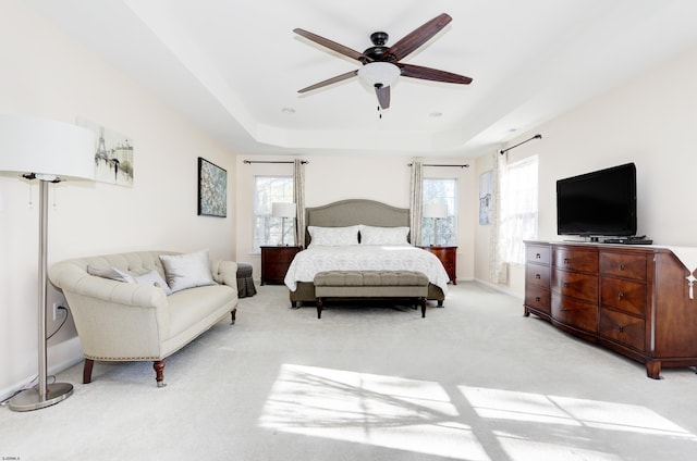 bedroom with light carpet, a tray ceiling, and ceiling fan