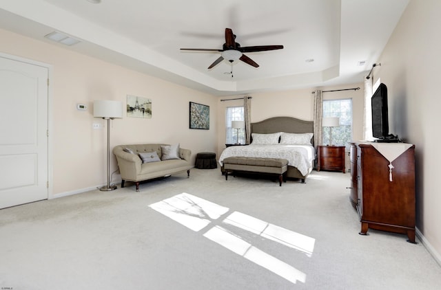 carpeted bedroom with ceiling fan, multiple windows, and a tray ceiling