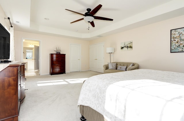 carpeted bedroom with ensuite bathroom, a raised ceiling, and ceiling fan