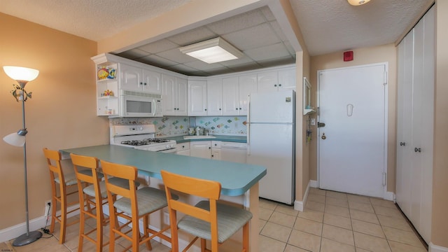 kitchen with tasteful backsplash, light tile patterned flooring, kitchen peninsula, white appliances, and white cabinets