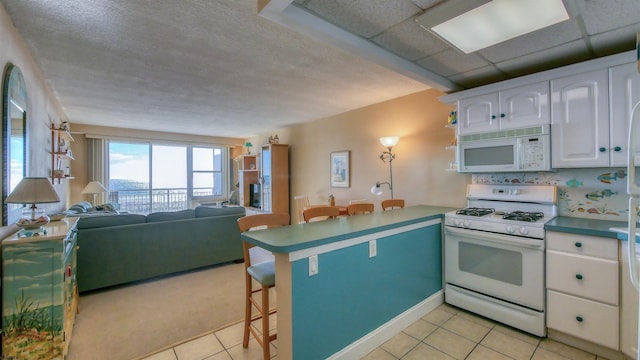 kitchen featuring a breakfast bar, white appliances, kitchen peninsula, light tile patterned flooring, and white cabinetry