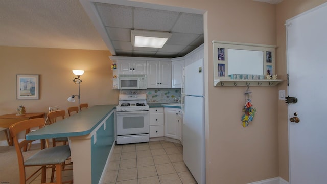 kitchen featuring a drop ceiling, white appliances, kitchen peninsula, white cabinetry, and a breakfast bar area