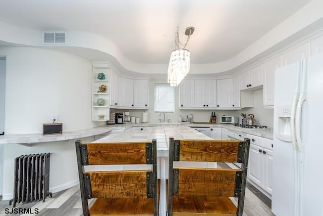 kitchen featuring white cabinetry, radiator heating unit, hanging light fixtures, white refrigerator with ice dispenser, and light wood-type flooring