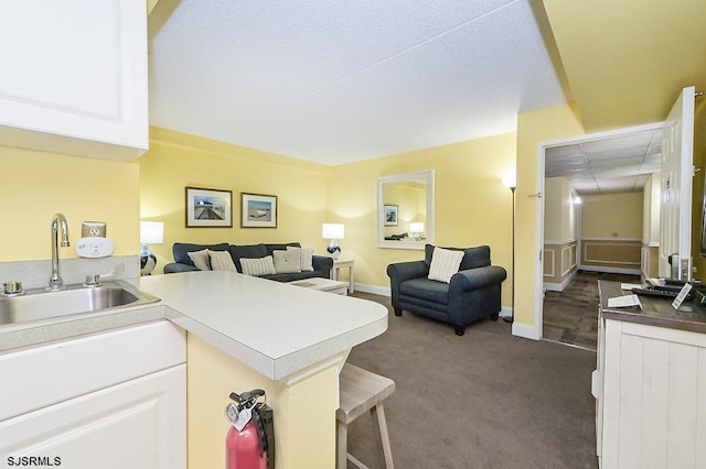 kitchen featuring kitchen peninsula, sink, white cabinets, and dark colored carpet