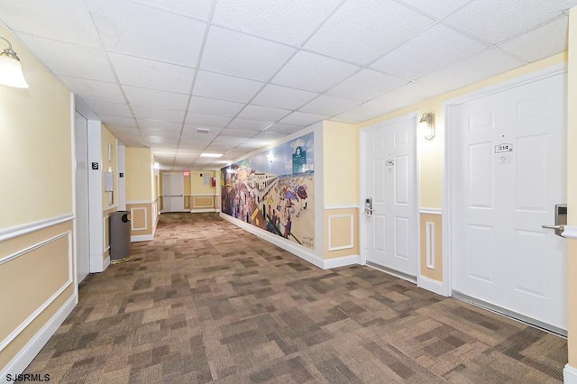 corridor with a drop ceiling and dark colored carpet