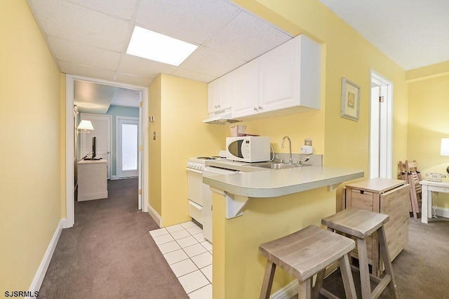 kitchen with a paneled ceiling, white cabinets, a kitchen breakfast bar, sink, and kitchen peninsula