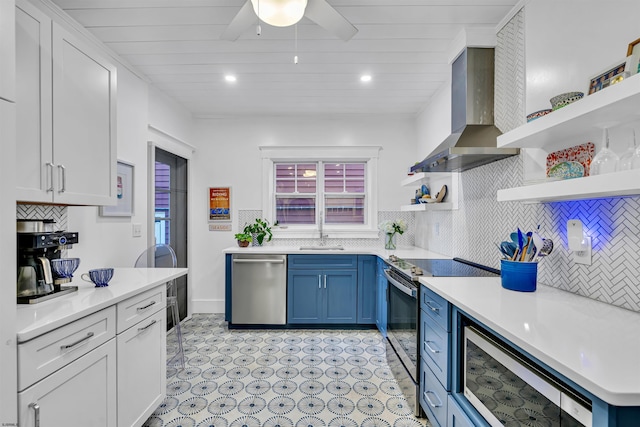 kitchen featuring white cabinets, wall chimney range hood, blue cabinets, and appliances with stainless steel finishes