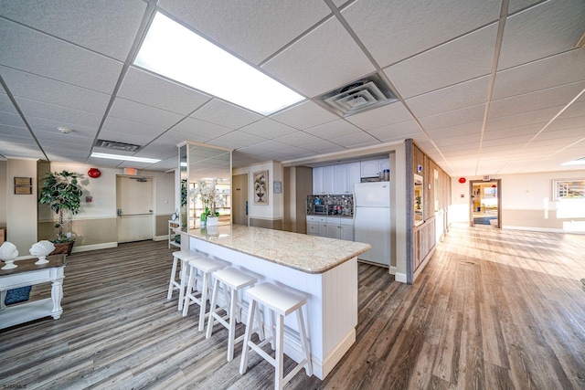 kitchen featuring white refrigerator, hardwood / wood-style flooring, light stone counters, and a breakfast bar area