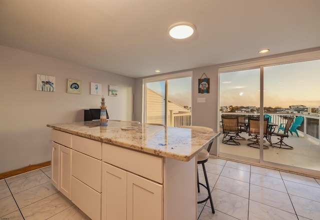 kitchen with a kitchen island, light stone counters, white cabinetry, and a breakfast bar area