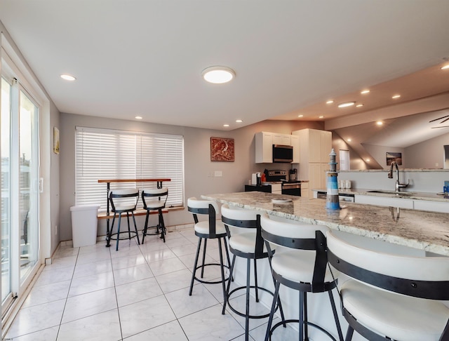 kitchen featuring a breakfast bar, sink, light stone counters, white cabinetry, and stainless steel appliances