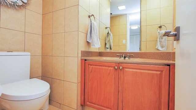 bathroom featuring vanity, toilet, and tile walls