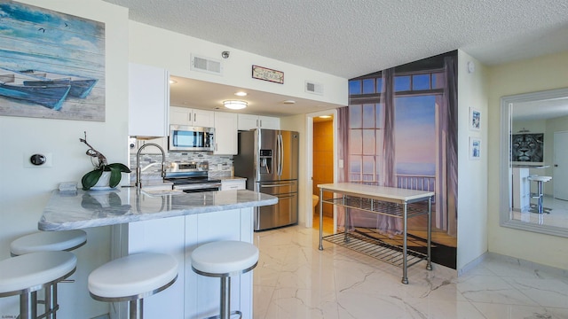 kitchen featuring white cabinetry, stainless steel appliances, kitchen peninsula, a textured ceiling, and decorative backsplash