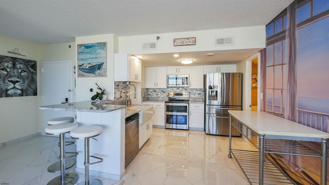 kitchen with kitchen peninsula, a textured ceiling, appliances with stainless steel finishes, tasteful backsplash, and white cabinetry