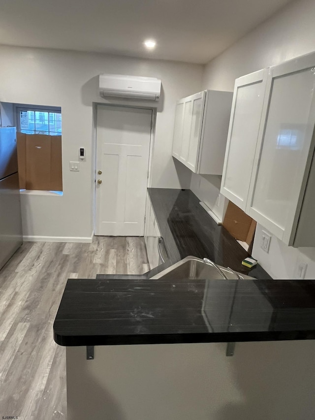 kitchen with white cabinetry, a wall unit AC, kitchen peninsula, stainless steel fridge, and light wood-type flooring