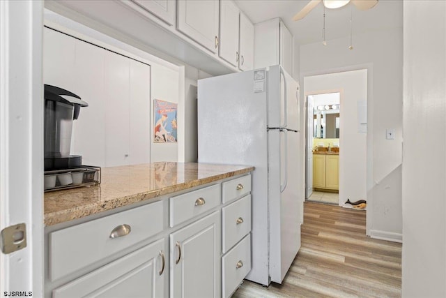 kitchen with light stone counters, white cabinets, light wood-type flooring, and white refrigerator