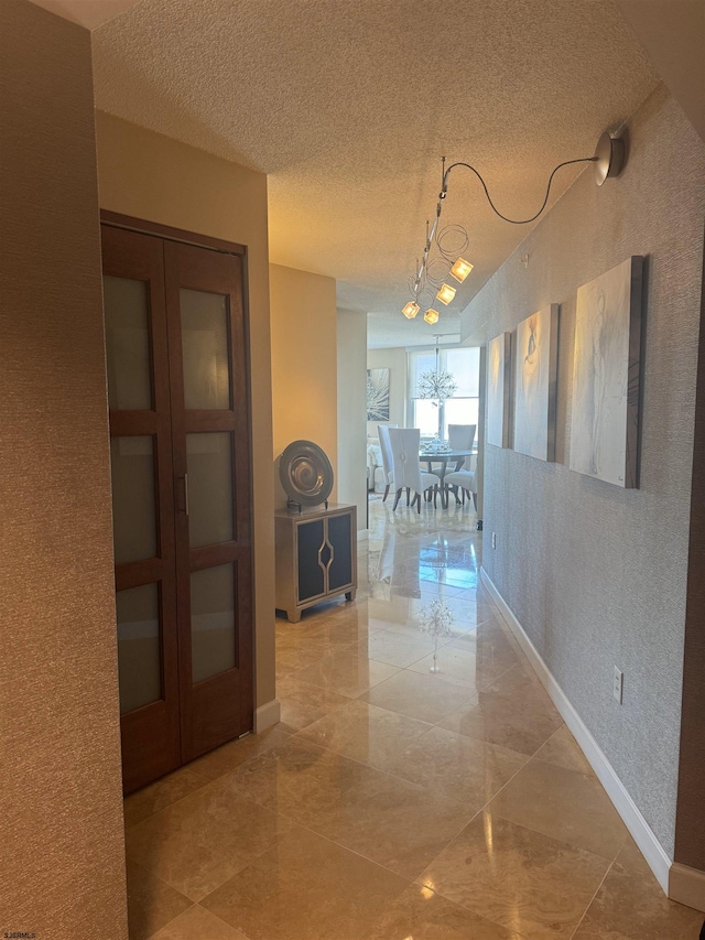 corridor with french doors, a textured ceiling, and a chandelier