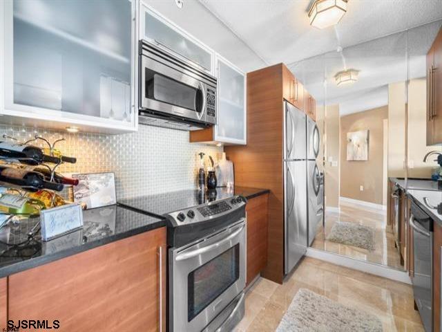 kitchen featuring tasteful backsplash, stainless steel appliances, stacked washer / dryer, and sink