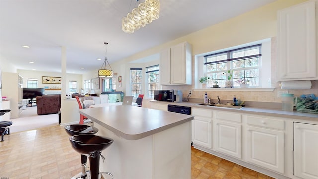 kitchen with hanging light fixtures, white cabinetry, a kitchen island, and sink