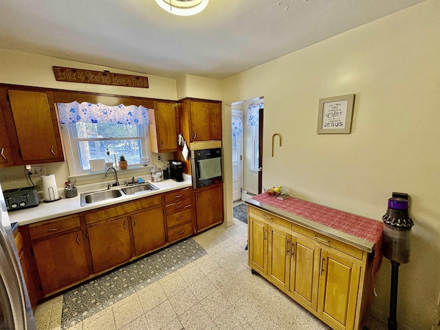 kitchen with brown cabinetry, oven, light countertops, light floors, and a sink