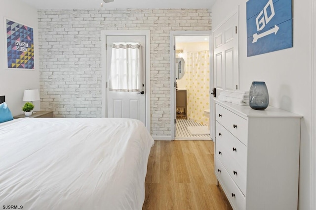 bedroom featuring connected bathroom, brick wall, and light wood-type flooring