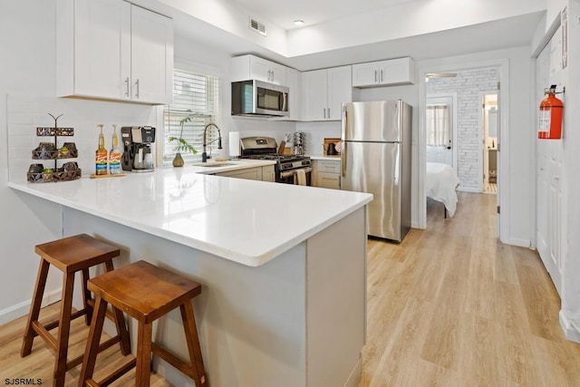 kitchen with sink, kitchen peninsula, a kitchen bar, white cabinetry, and stainless steel appliances