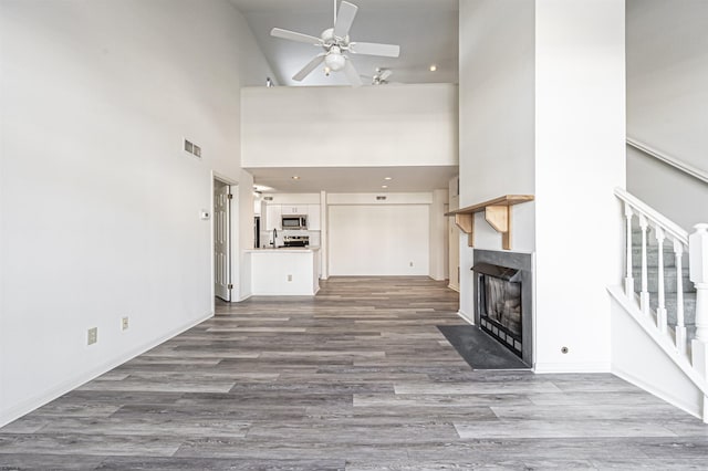 unfurnished living room featuring wood-type flooring, high vaulted ceiling, and ceiling fan