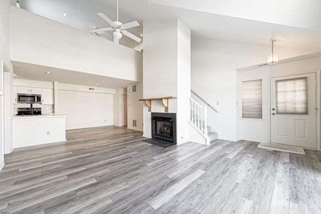 unfurnished living room with ceiling fan, light hardwood / wood-style floors, and high vaulted ceiling