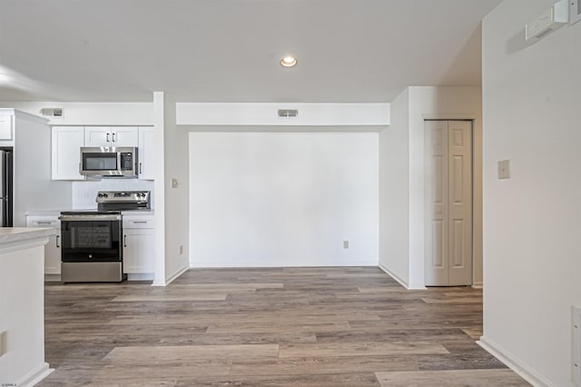 kitchen with backsplash, white cabinetry, stainless steel appliances, and light hardwood / wood-style flooring