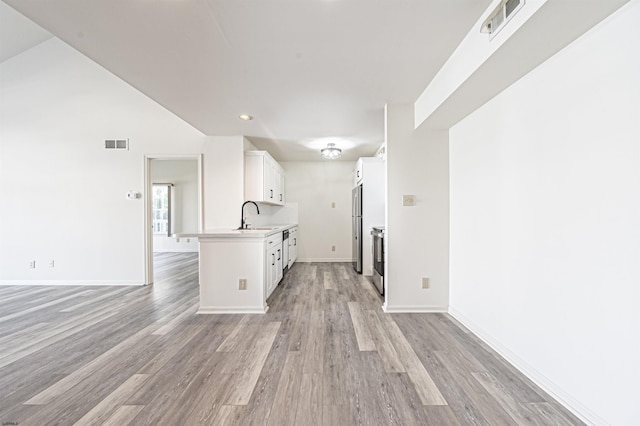 kitchen with white cabinets, sink, light wood-type flooring, kitchen peninsula, and stainless steel refrigerator