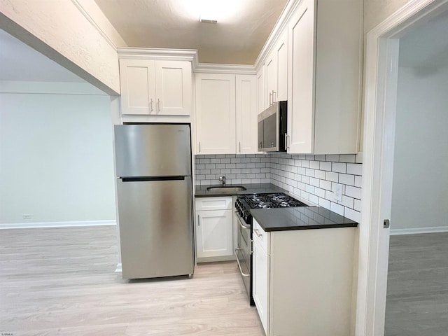 kitchen featuring white cabinetry, sink, stainless steel appliances, light hardwood / wood-style flooring, and backsplash