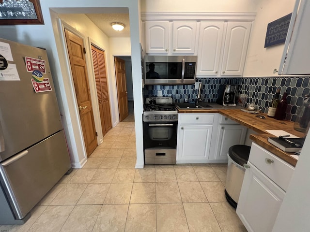 kitchen featuring white cabinets, light tile patterned floors, tasteful backsplash, butcher block counters, and stainless steel appliances