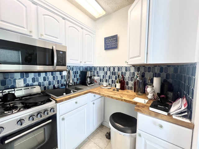 kitchen with white cabinets, gas stove, butcher block counters, and backsplash