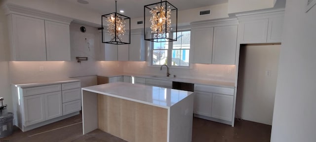 kitchen featuring visible vents, a kitchen island, decorative light fixtures, white cabinetry, and a sink