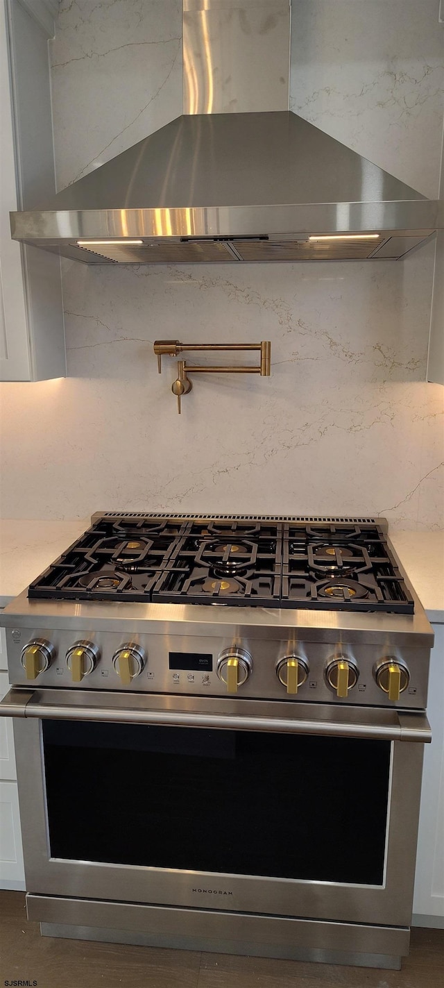 room details featuring stainless steel stove, white cabinets, light countertops, wall chimney exhaust hood, and backsplash