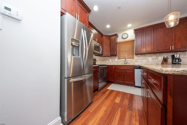 kitchen featuring pendant lighting, sink, decorative backsplash, light stone countertops, and appliances with stainless steel finishes