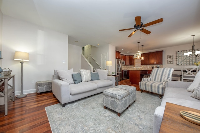 living room featuring ceiling fan with notable chandelier and dark wood-type flooring