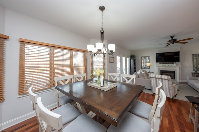 dining area with a tile fireplace, ceiling fan with notable chandelier, and dark hardwood / wood-style floors