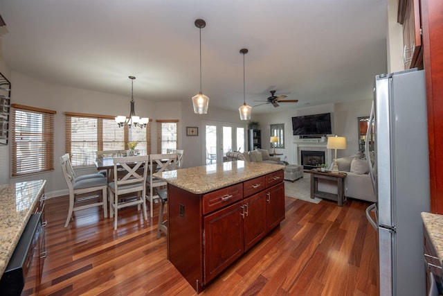 kitchen with light stone countertops, stainless steel fridge, ceiling fan with notable chandelier, pendant lighting, and a center island