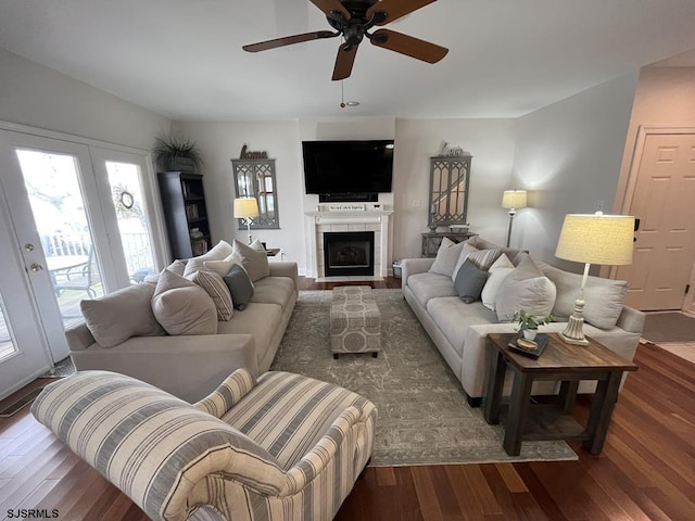 living room featuring a tiled fireplace, ceiling fan, and dark wood-type flooring